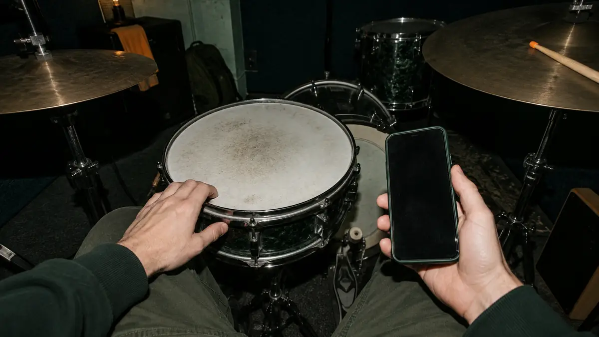 Un telefono in una mano, la seconda mano sul cerchio del rullante, in una sala prove con le pareti di moquette blu